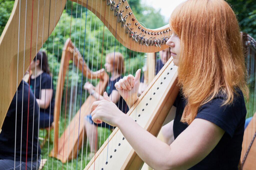 Une jeune femme rousse joue de la harpe avec d'autre musiciens.