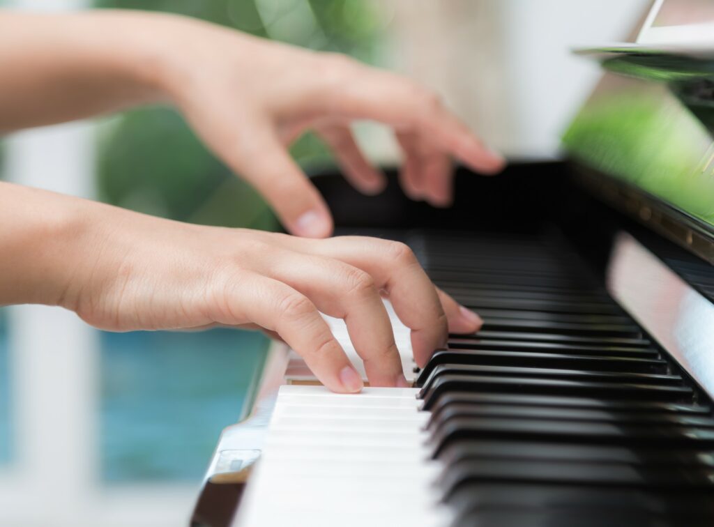 Vue de deux mains qui jouent une partition sur un piano.