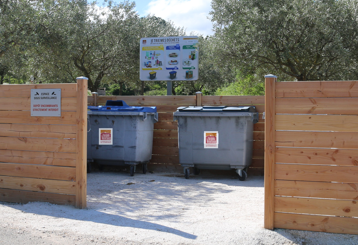 Vue de deux bacs à couvercle bleu installés sur un point d'apport volontaire de déchets.